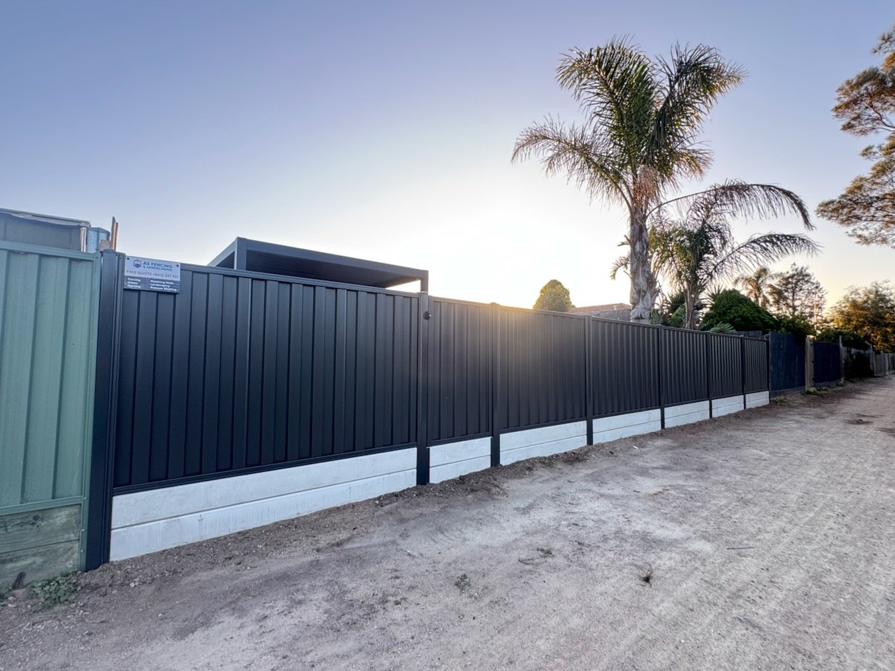 Finished Colorbond fence with an AS Fencing sign on it, at dusk