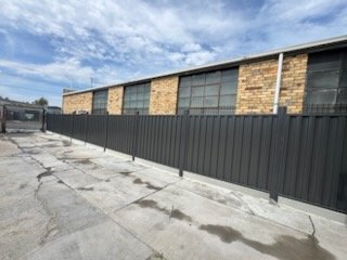 Long dark Colorbond fence beside a brick warehouse